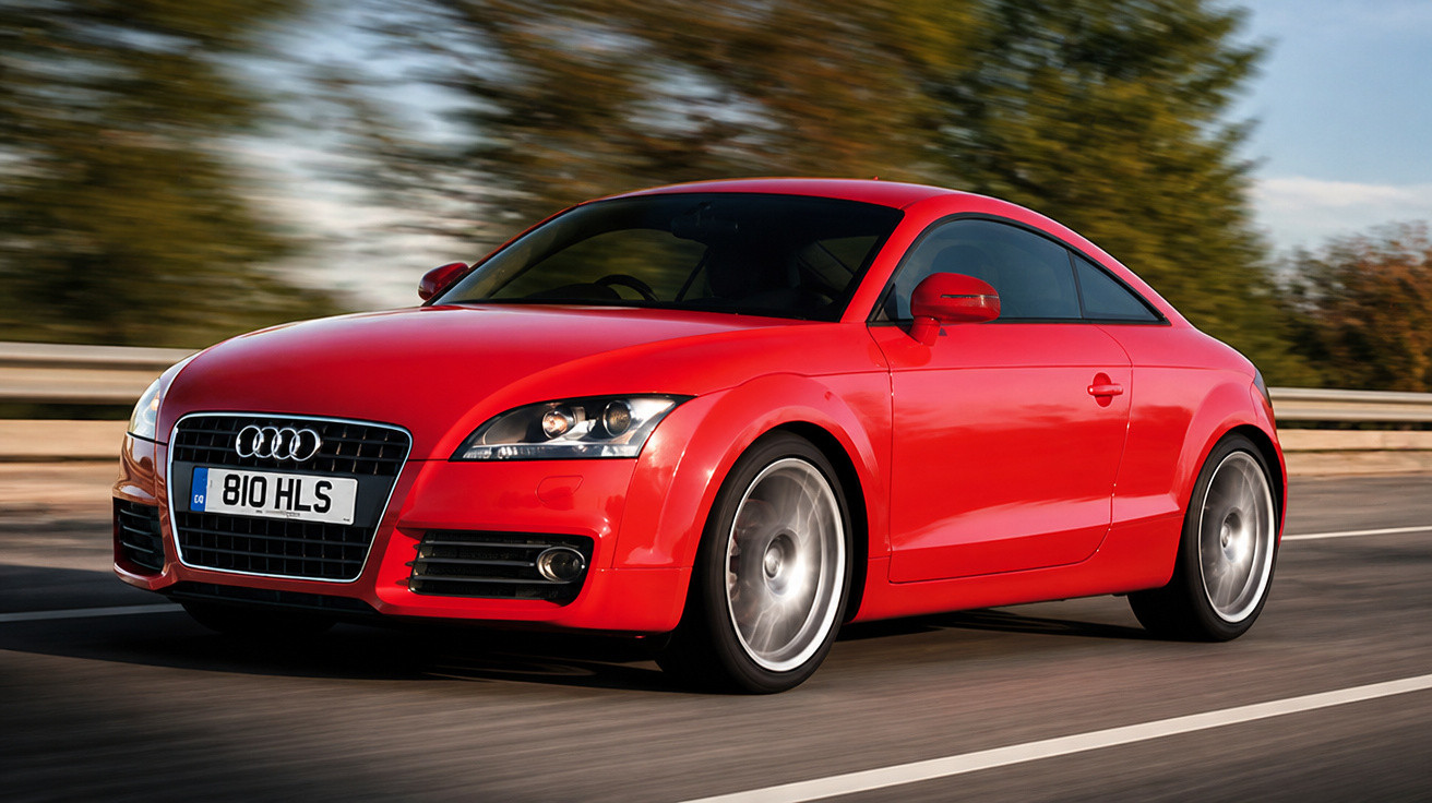 Roter Audi TT Sportwagen fährt auf einer Straße mit Bäumen im Hintergrund an einem sonnigen Tag.
