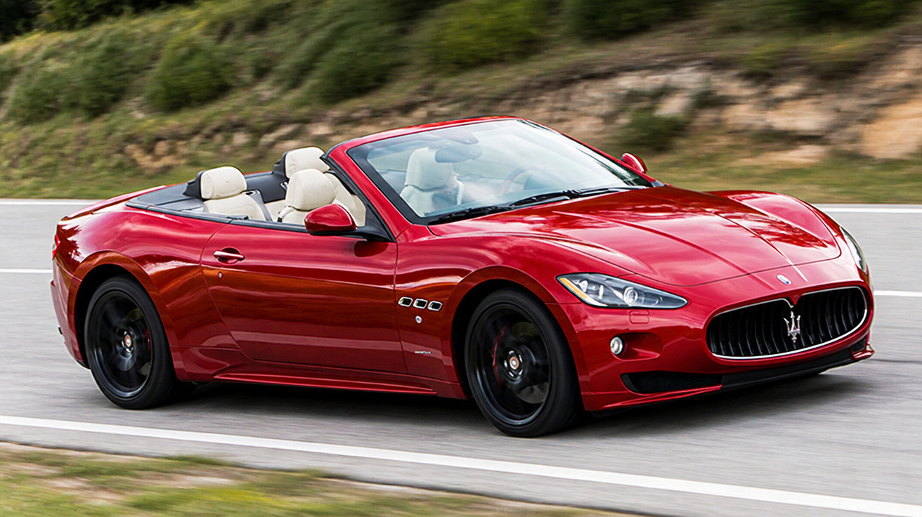 Roter Maserati Sportwagen Cabrio fährt schnell auf kurviger Bergstrasse, helle Sitze, grüne Landschaft.