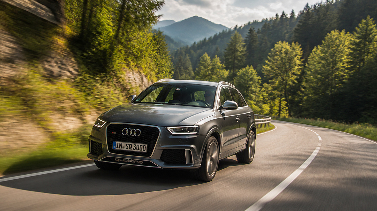 Audi SQ5 fährt auf kurviger Bergstrasse, umgeben von Wald und bewölktem Himmel.